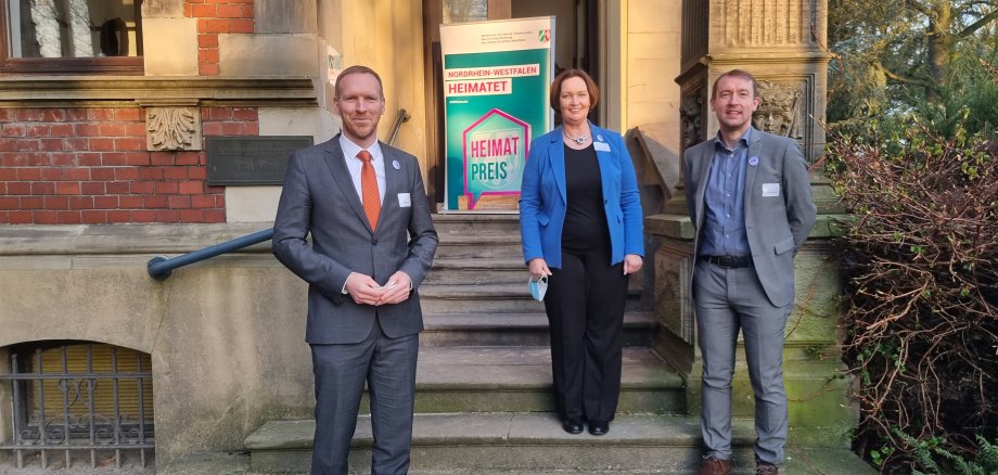 NRW-Staatssekretär Dr. Jan Heinisch, Bürgermeisterin Christa Lenderich und Wirtschaftsförderer Robert Tausewald vor der Villa Winkel mit dem Heimatpreis-Banner