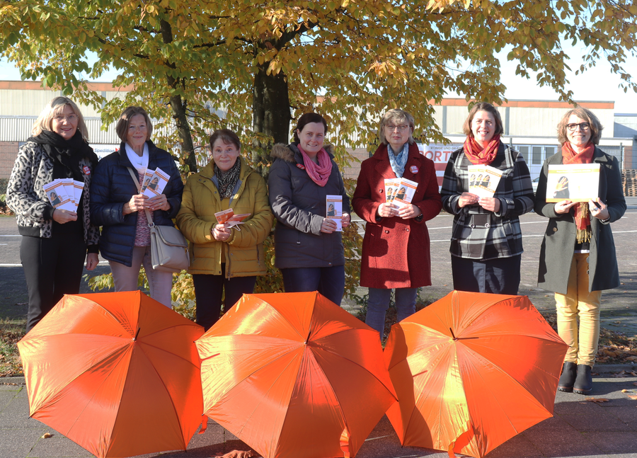 Sie sehen hinter aufgespannten orangen Schirmen (v.l.) Birgit Schmale-Borgers (Soroptimistinnen), Renate Winter, Gertrud Kubitza (ev. Frauenhilfe), Annemarie Möhring (Miteinander e.V.), Pfarrerin Heike Bergmann, Gleichstellungsbeauftragte Julie Nacke und Elke Wolf (OST)