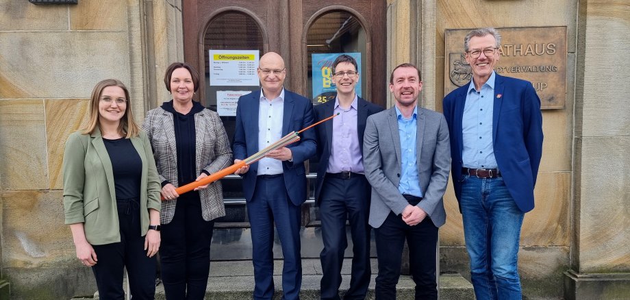 Sie sehen: Personen vor dem Ochtruper Rathaus mit Glasfaserkabel (Lisa Scheidle (epcan), Bürgermeisterin Christa Lenderich, Landrat Dr. Martin Sommer, Ingmar Ebhardt (WESt), Wirtschaftsförderer Robert Tausewald und Kämmerer Roland Frenkert)