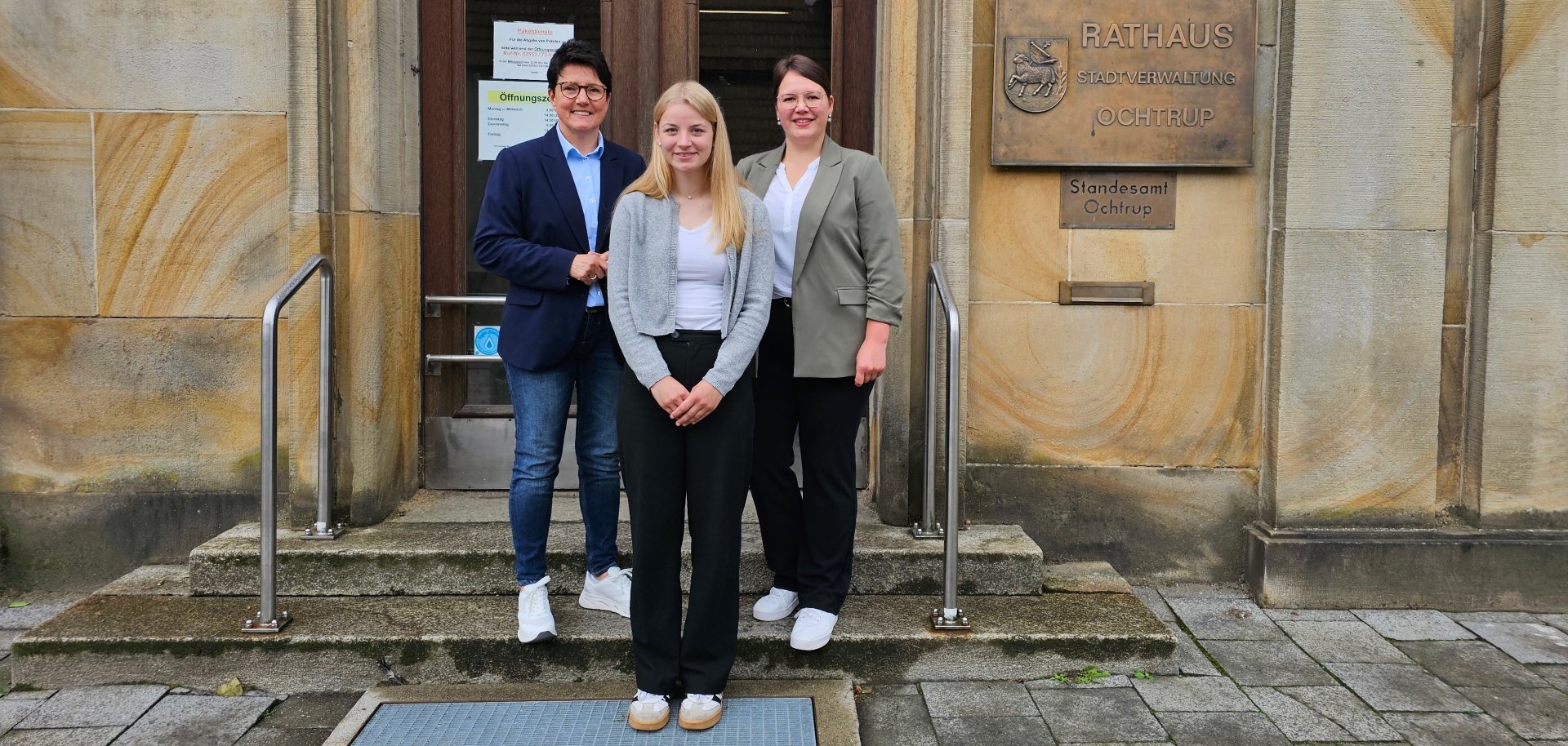Sie sehen: drei Personen vor der Eingangstür des Ochtruper Rathauses