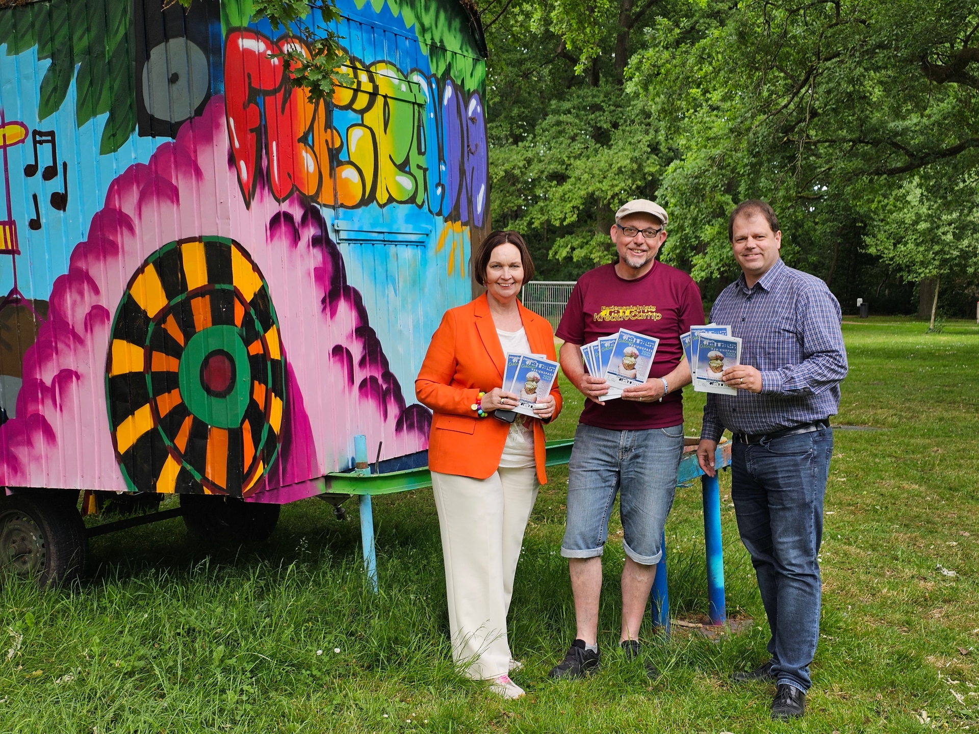Sie sehen: eine Personengruppe vor einem bunten Bauwagen (Bürgermeisterin Christa Lenderich, Jörg Eßlage vom Jugendcafé Freiraum und VHS-Leiter Timo Lobbel).