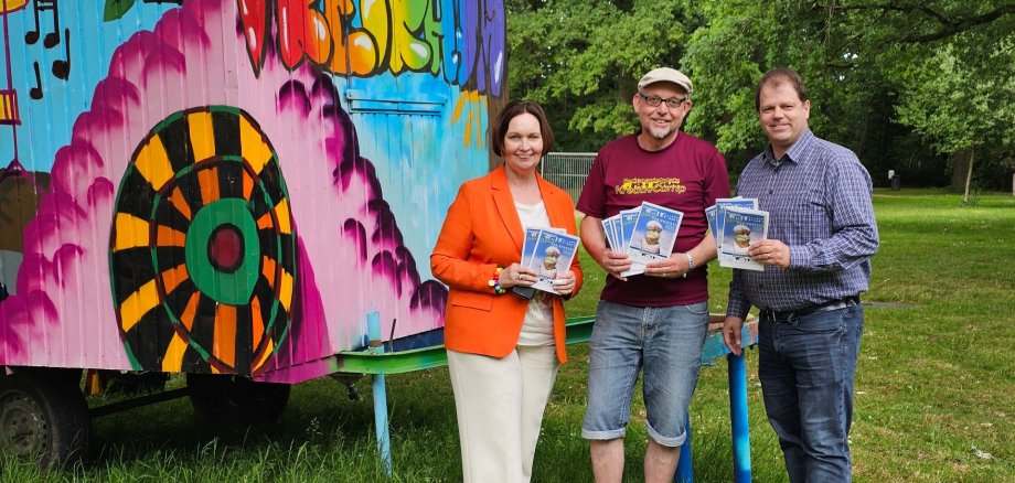 Sie sehen: eine Personengruppe vor einem bunten Bauwagen (Bürgermeisterin Christa Lenderich, Jörg Eßlage vom Jugendcafé Freiraum und VHS-Leiter Timo Lobbel).