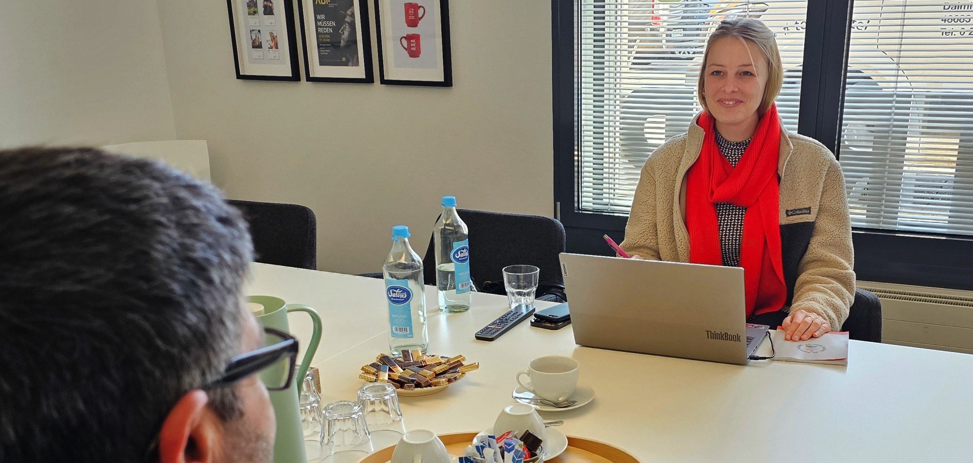 Sie sehen: Personen gegenüber an einem Tisch mit Laptop