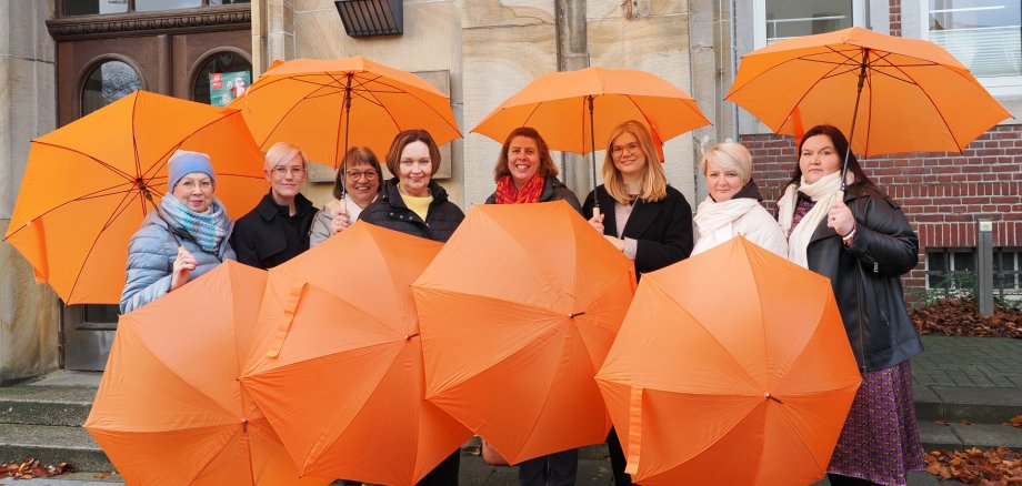 Sie sehen: Eine Personengruppe mit oraangefarbenen Schirmen