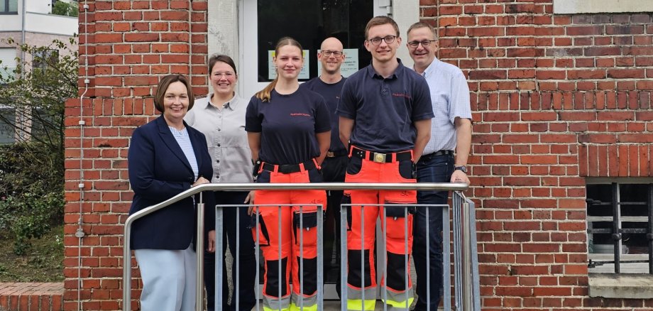 Sie sehen: eine Personengruppe auf der Treppe vor dem Rathaus.