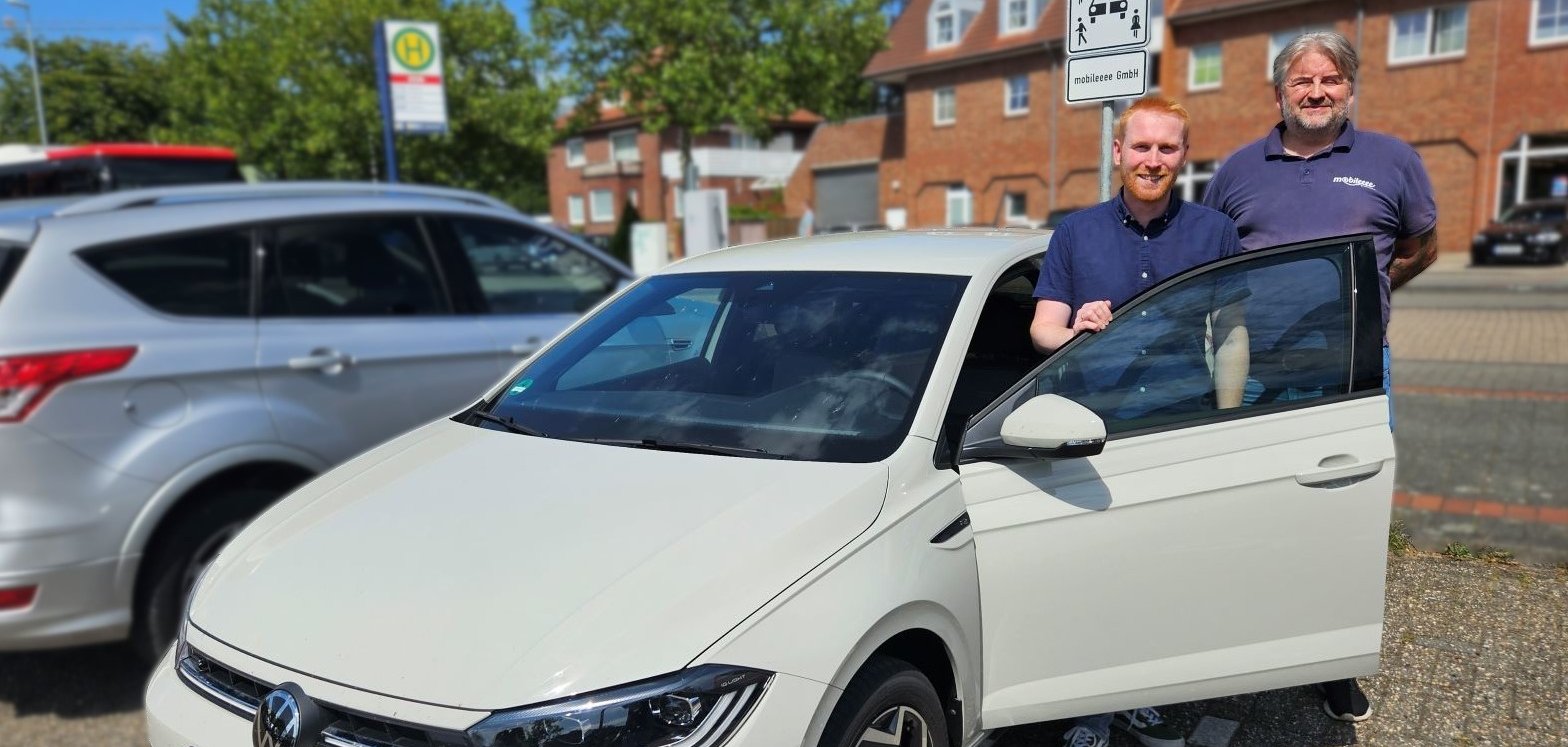 Sie sehen: zwei Personen neben einem parkenden Kleinwagen