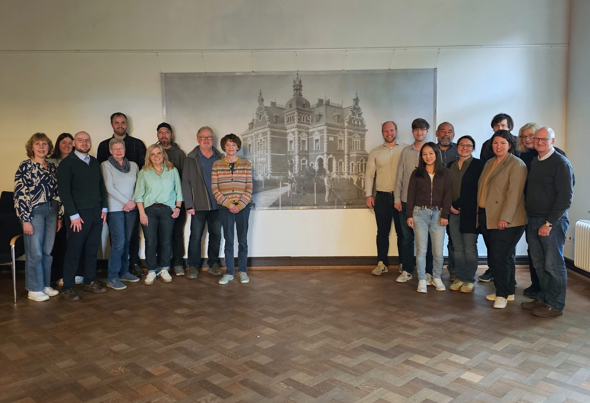 Sie sehen: eine Personengruppe vor einem historischen Bild mit der Villa Winkel