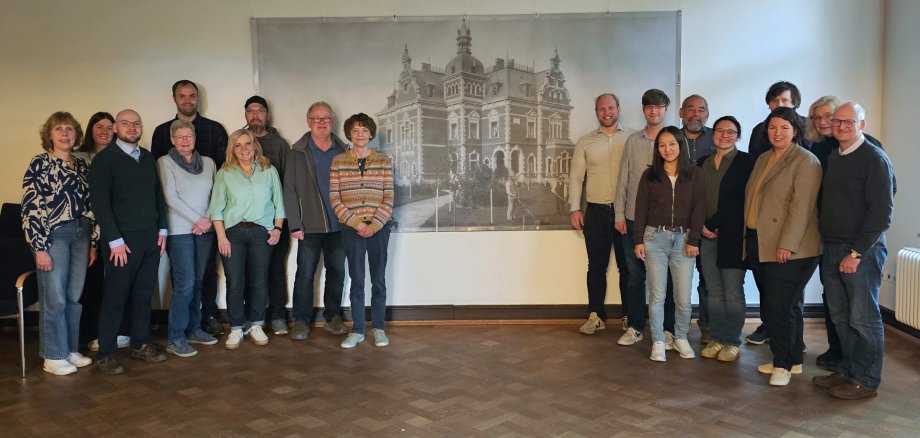 Sie sehen: eine Personengruppe vor einem historischen Bild mit der Villa Winkel