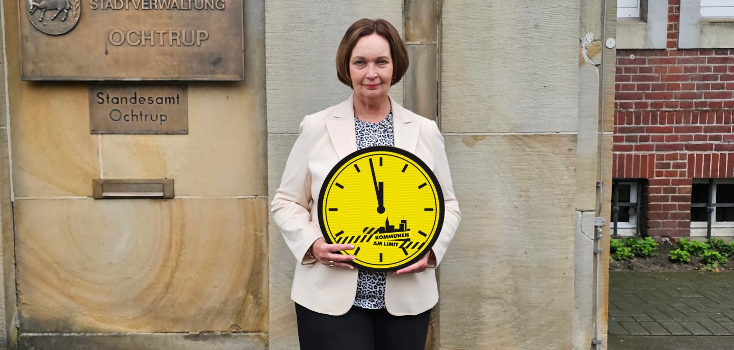 Sie sehen: Bürgermeisterin Christa Lenderich mit einer gelben Uhr, die kurz vor zwölf anzeigt.