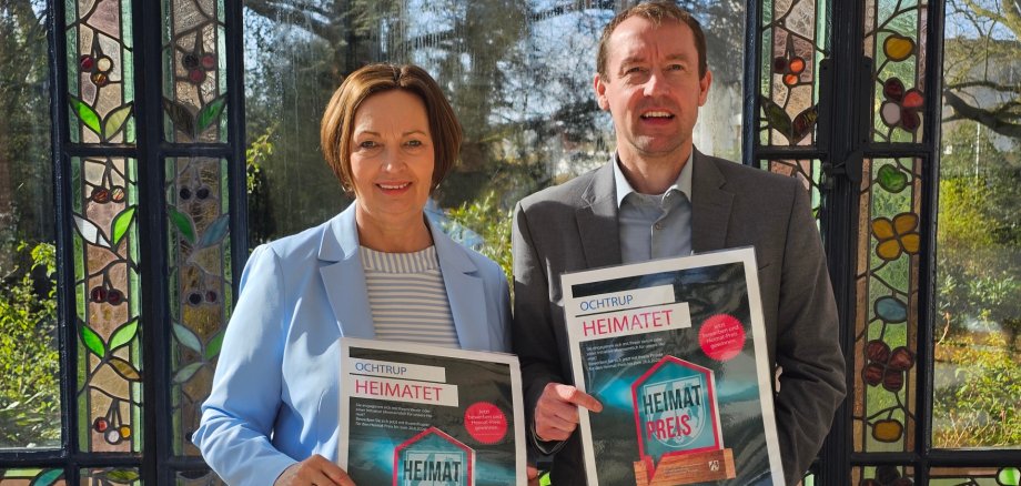 Sie sehen: zwei Personen mit einem Plakat zum Heimatpreis in den Händen.