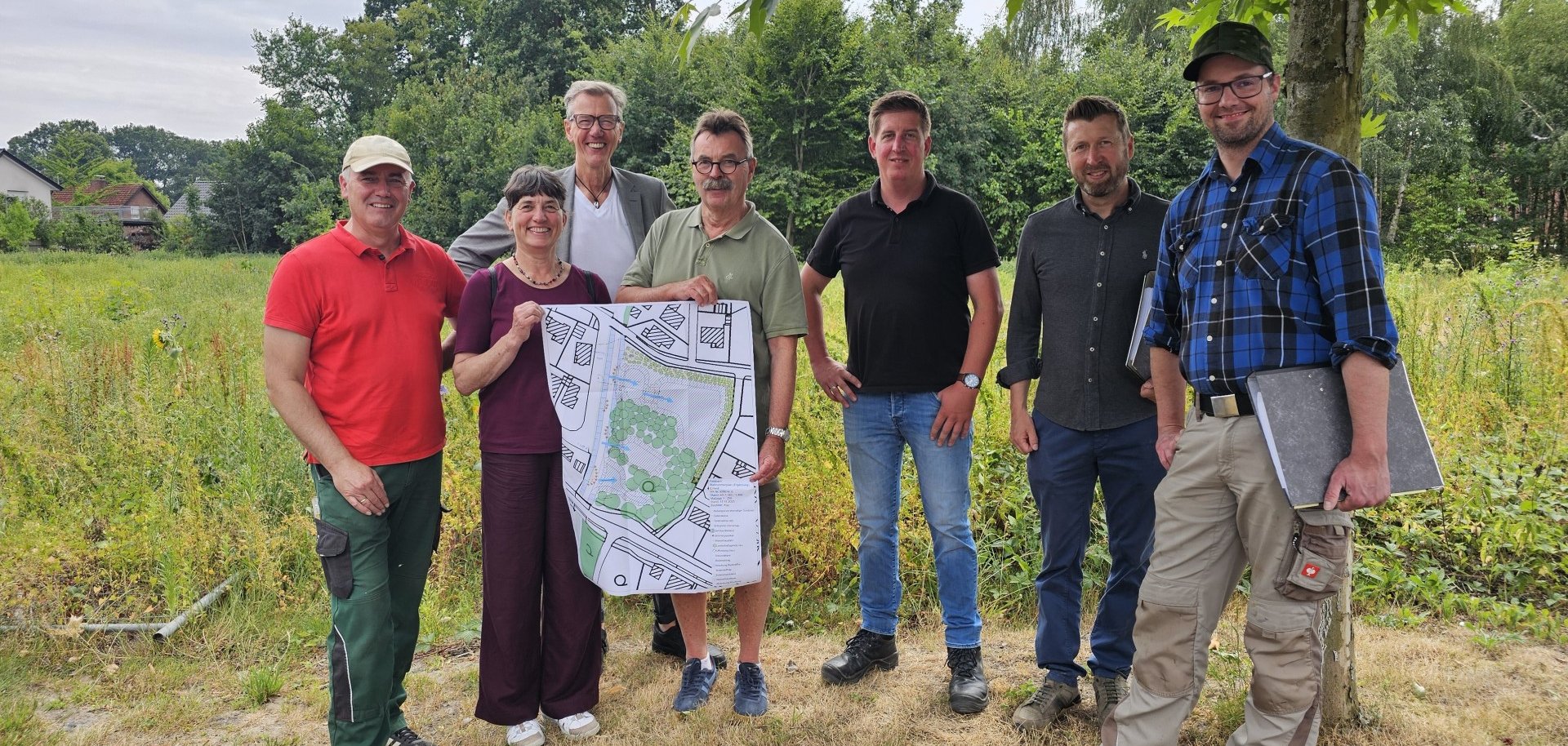 Sie sehen: eine Personengruppe mit einer Planskizze vor der geplanten Retentionsfläche. 