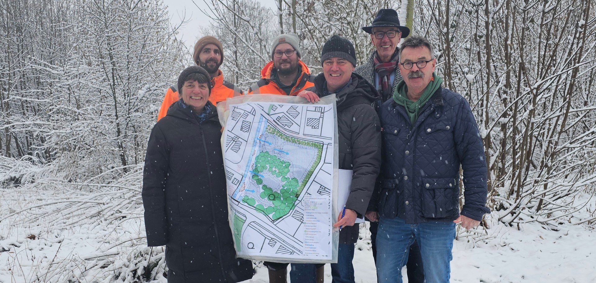 Sie sehen: eine Personengruppe mit einer Planskizze vor einer verschneiten Landschaft