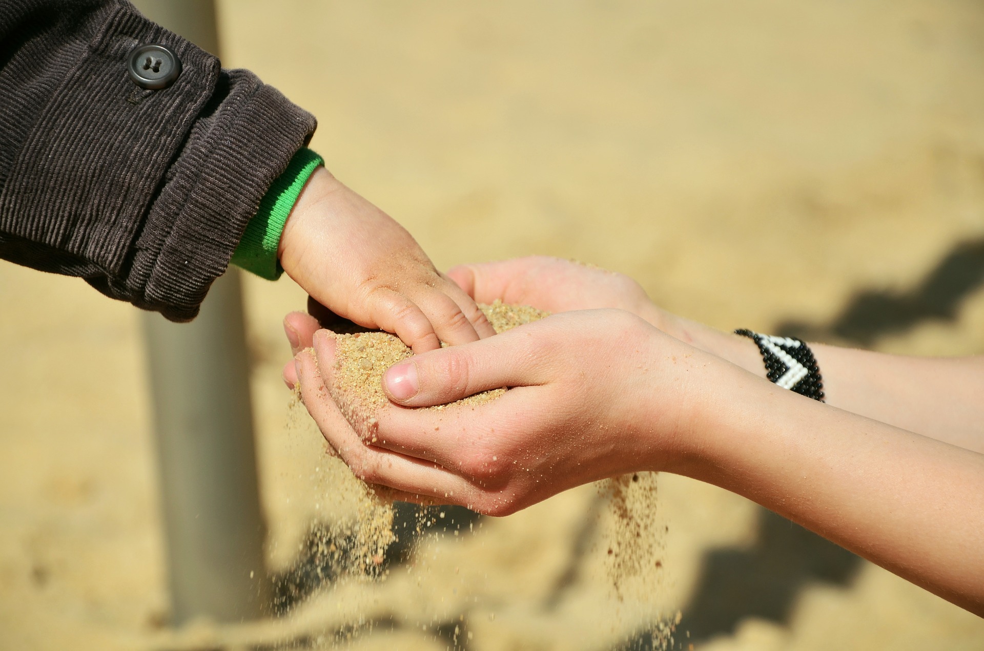 Kinderhand, die Sand aus Erwachsenenhänden schöpft