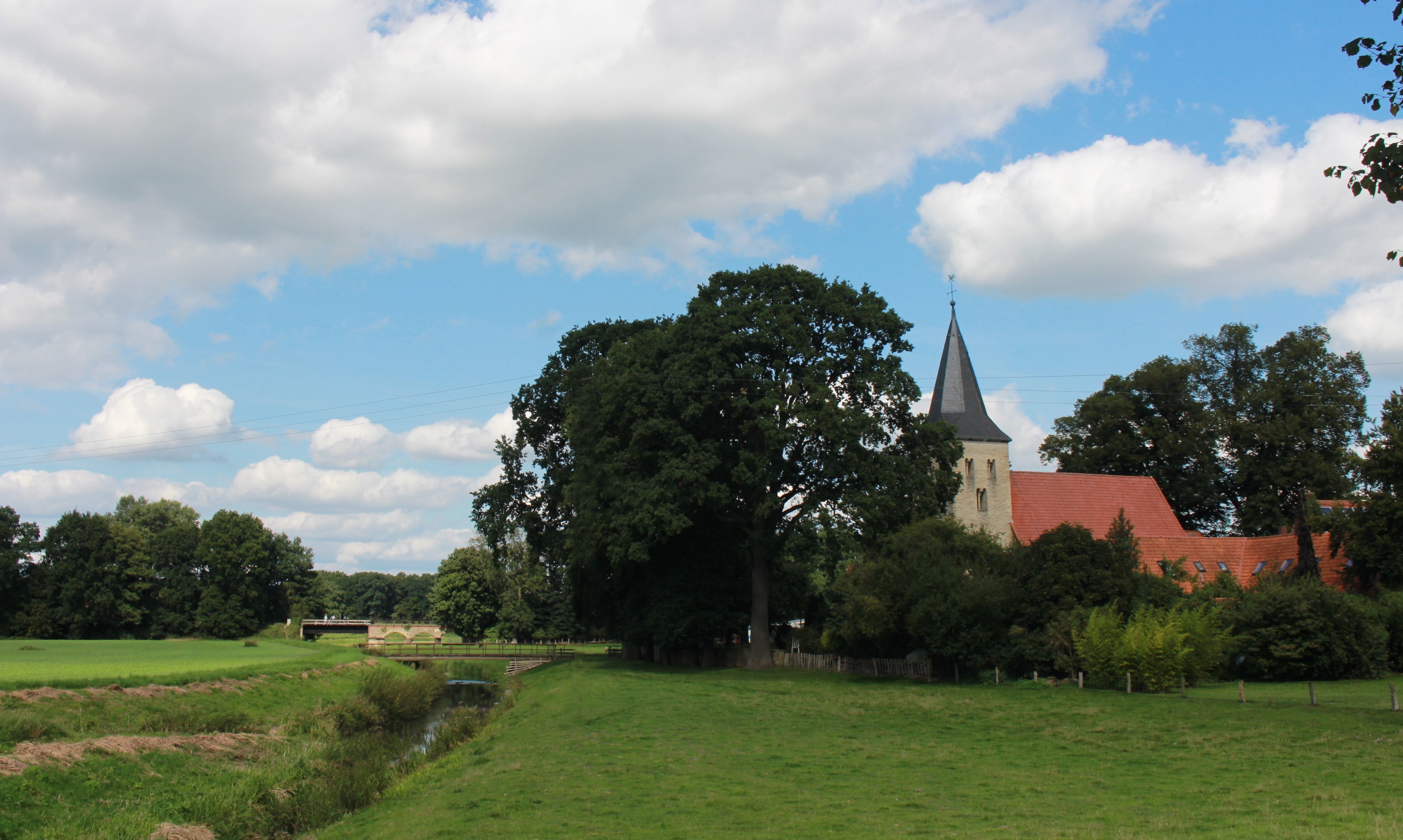 Blick auf die Alte Kirche von Welbergen hinter einer Baumgruppe und Vechtebrücke im Hintergrund