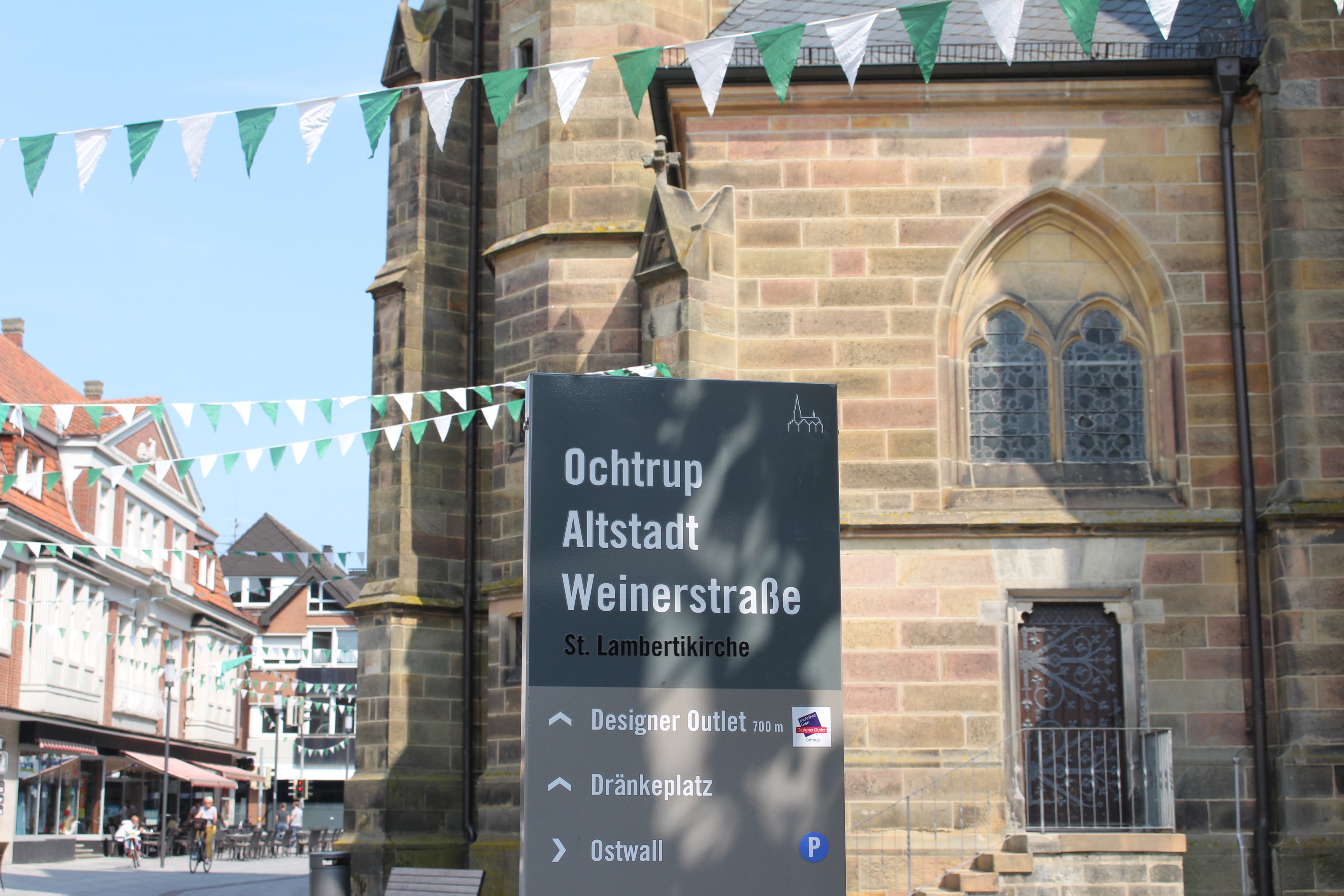 Sie sehen: ein Schild mit den Gemäuern der Lambertikirche im Hintergrund