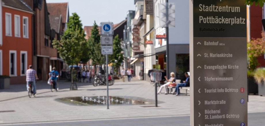 Sie sehen: den Blick in eine Fußgängerzone (Pottbäckerplatz) mit Infotafel
