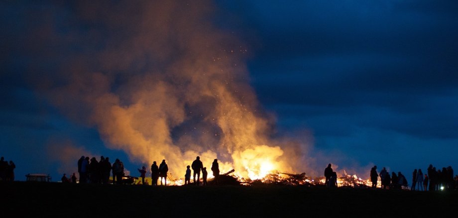 Sie sehen: die Silhouetten von Menschen vor einem Osterfeuer