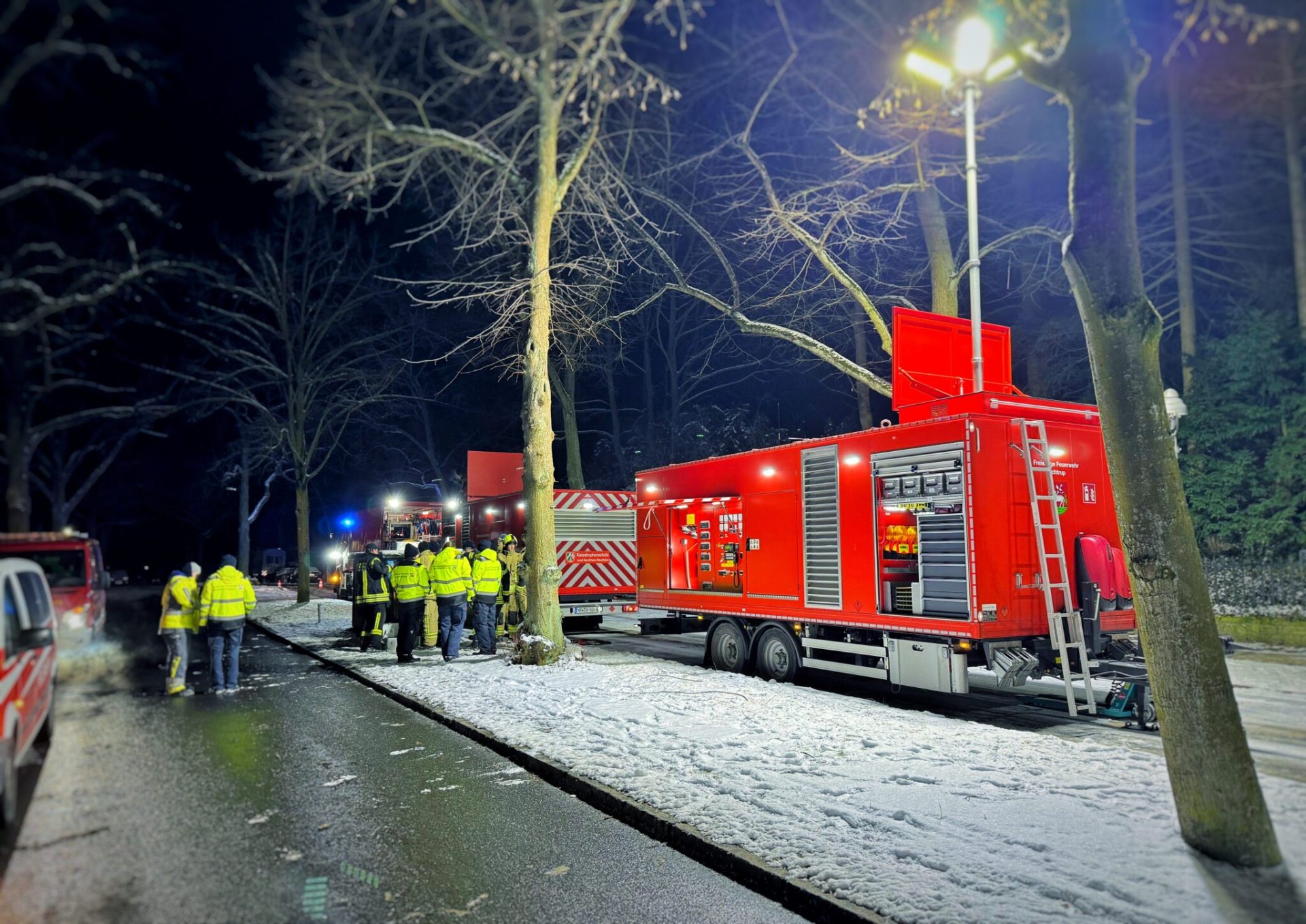 Sie sehen: Einsatzkräfte neben Feuerwehrwagen 