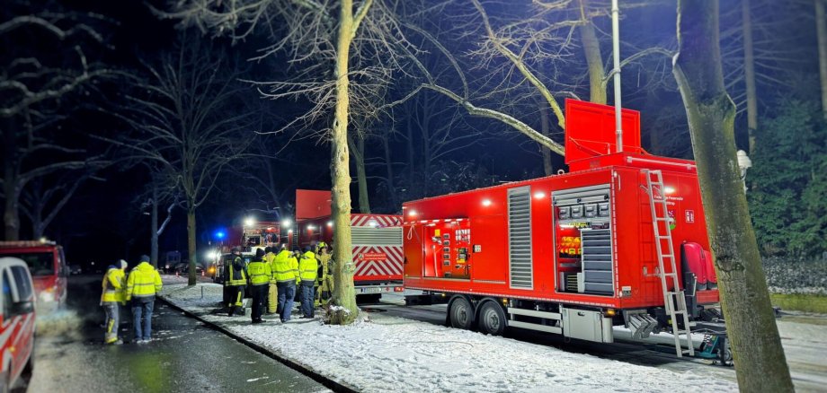 Sie sehen: Einsatzkräfte neben Feuerwehrwagen
