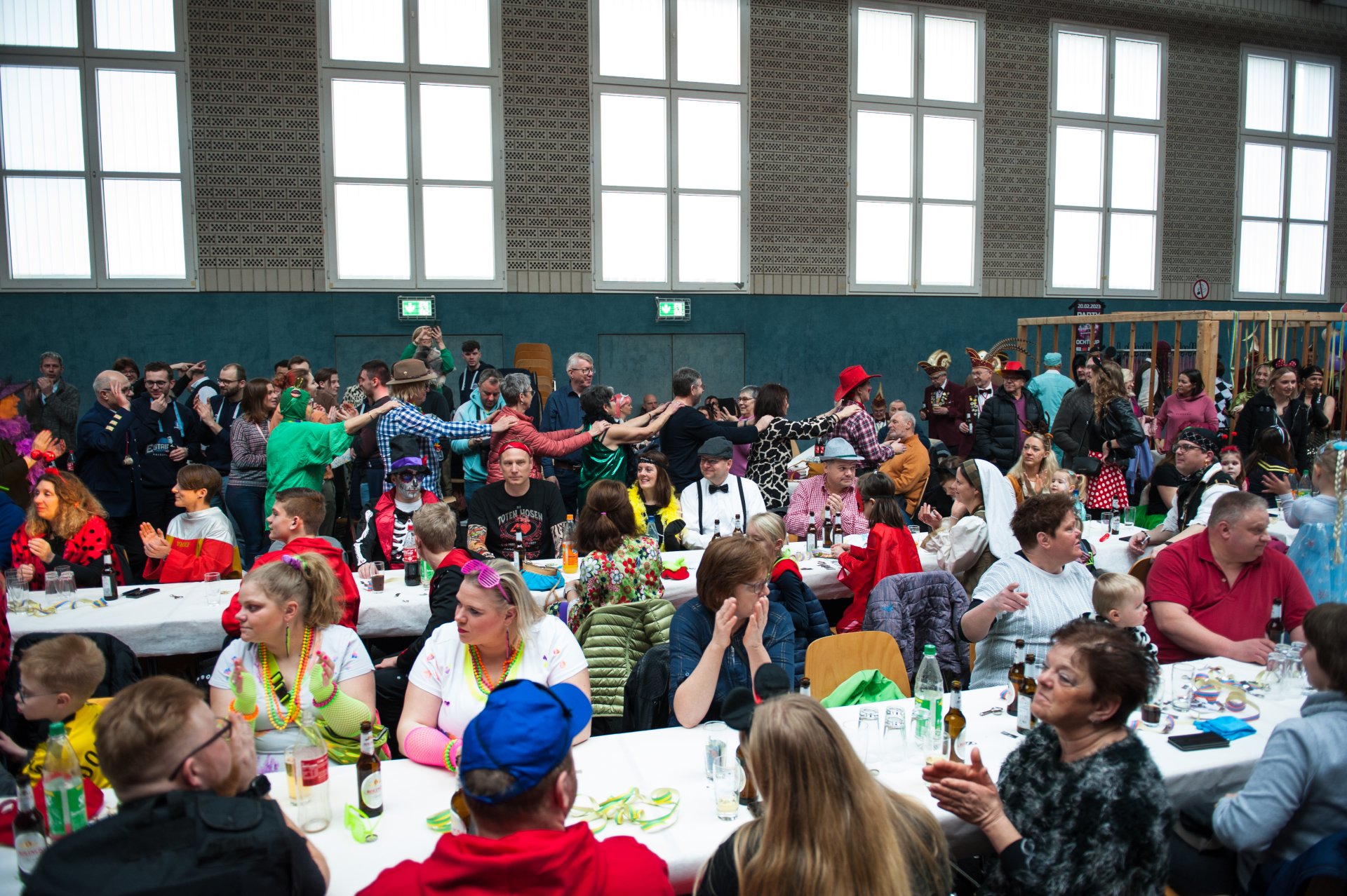 Sie sehen: Menschen an Tischreihen bei einer Karnevalsparty 
