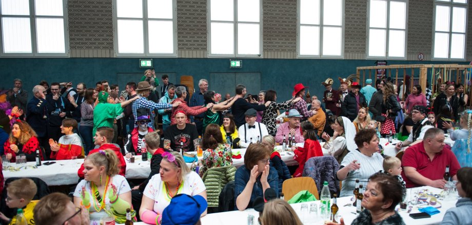 Sie sehen: Menschen an Tischreihen bei einer Karnevalsparty 