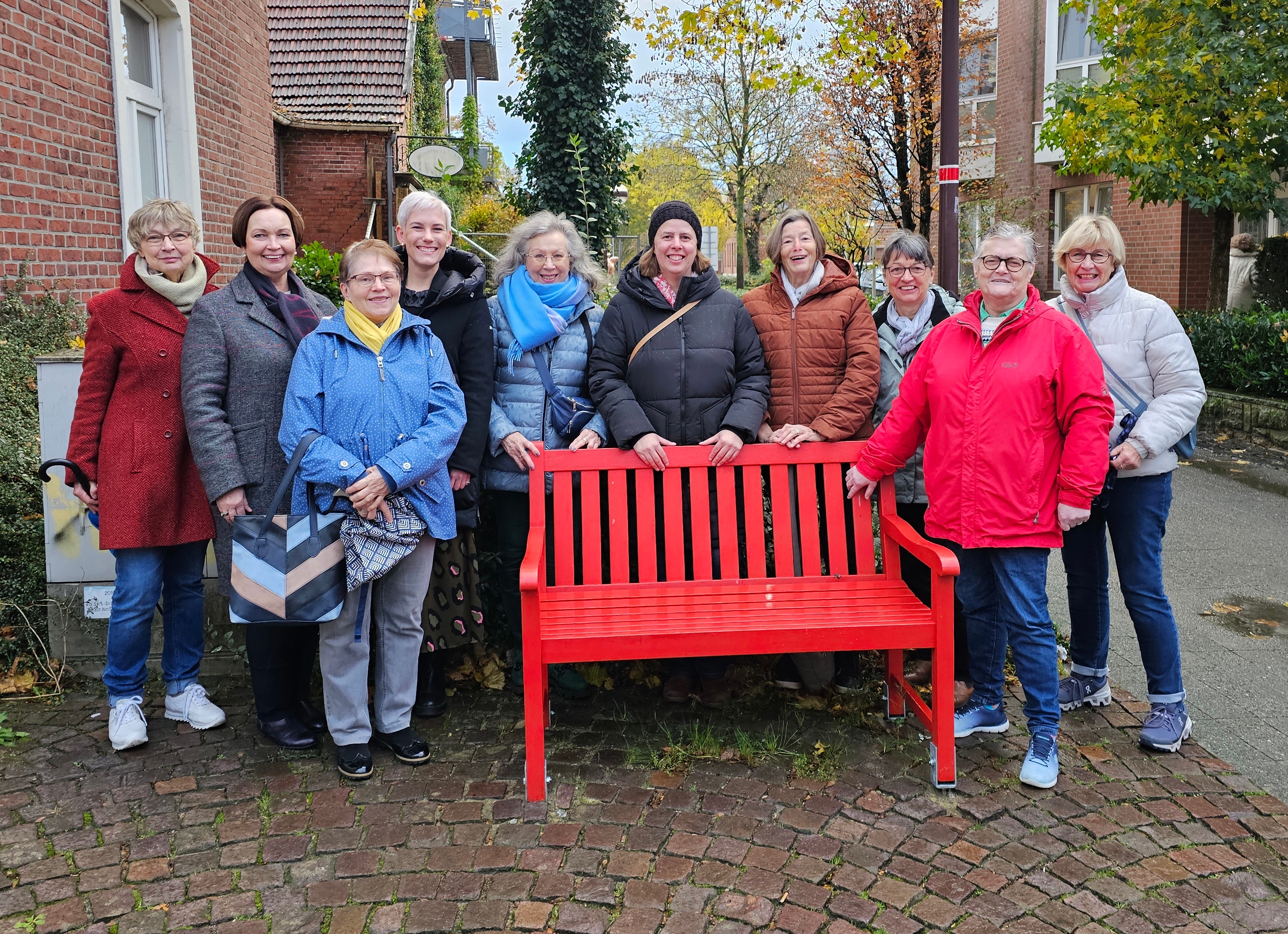 Se sehen: eine Gruppe von Personen an einer roten Bank. Es handelt sich um Mitglieder des Ochtruper Frauennetzwerkes.