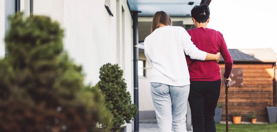 Sie sehen: Eine Pflegerin unterstützt eine ältere Frau beim Laufen