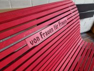 Sie sehen: die Lehne einer roten Bank mit der Aufschrift "von Frauen für Frauen"