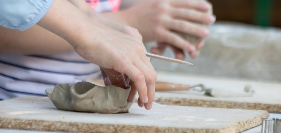 Sie sehen: Kinderhände beim Formen von Ton