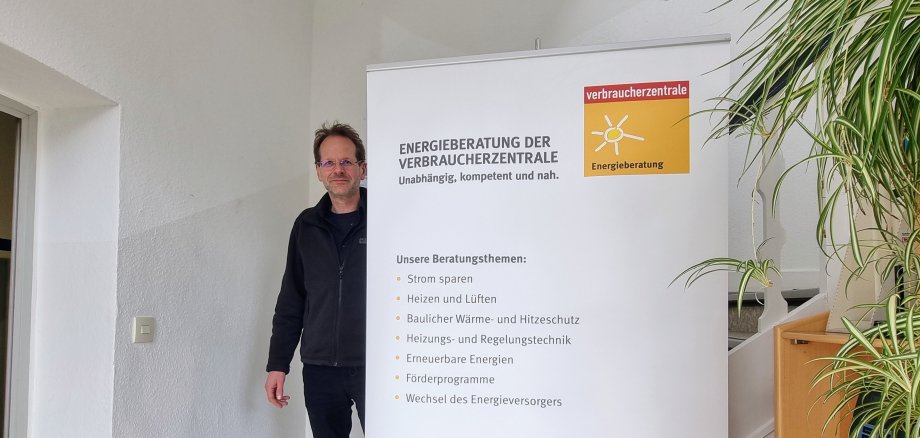 Sie sehen: eine Person an einem Roll-Up mit Infos der Verbraucherzentrale