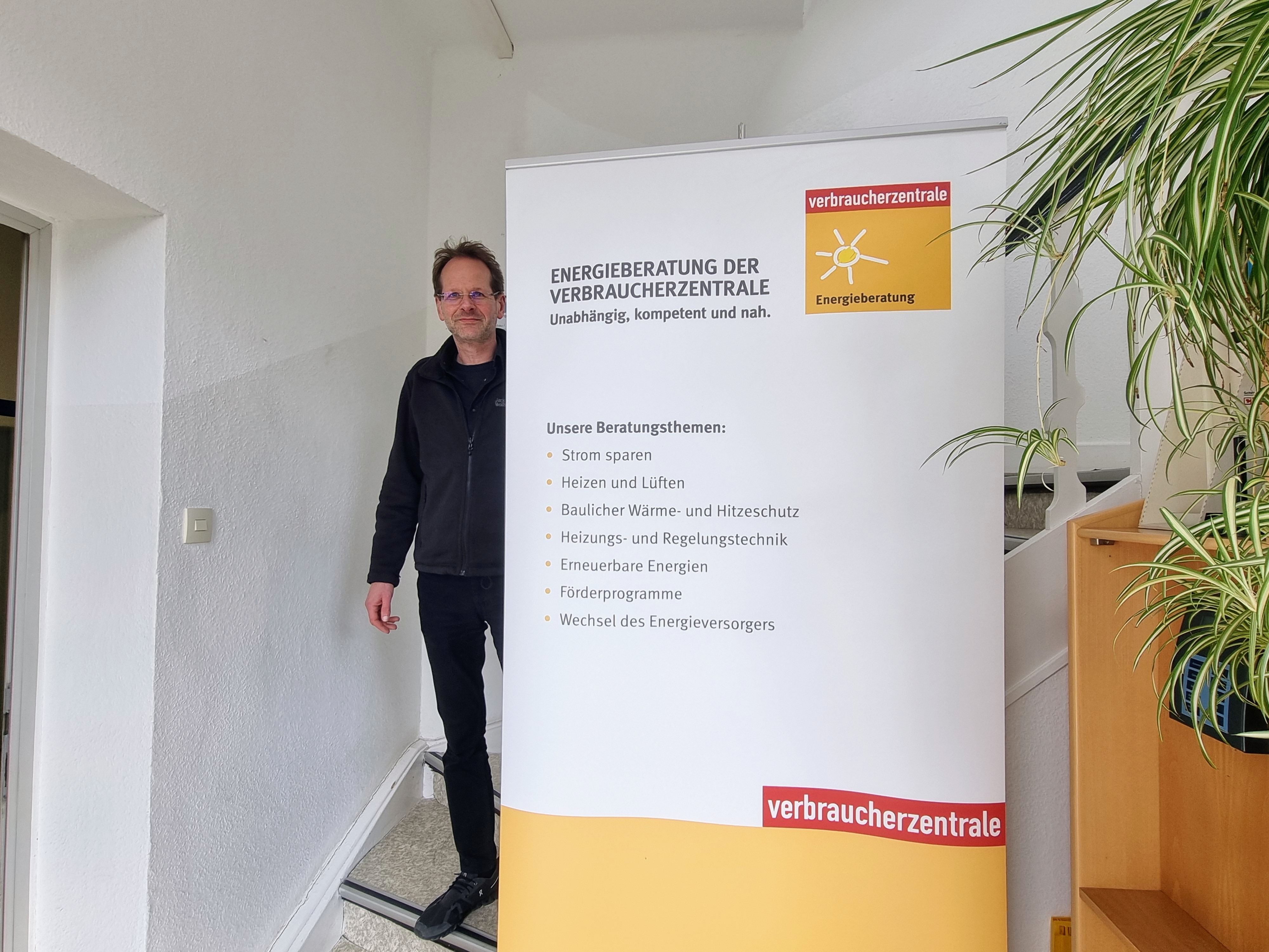 Sie sehen: eine Person an einem Roll-Up mit Infos der Verbraucherzentrale