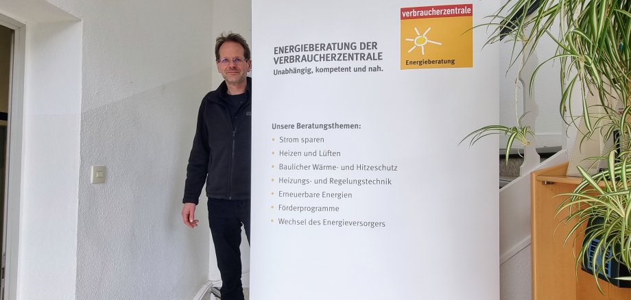 Sie sehen: eine Person an einem Roll-Up mit Infos der Verbraucherzentrale