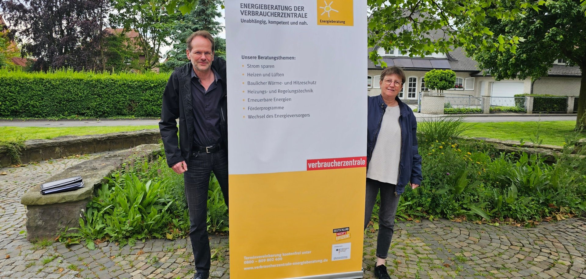 Sie sehen: Zwei Personen mit einem Banner der Verbraucherzentrale in ihrer Mitte.