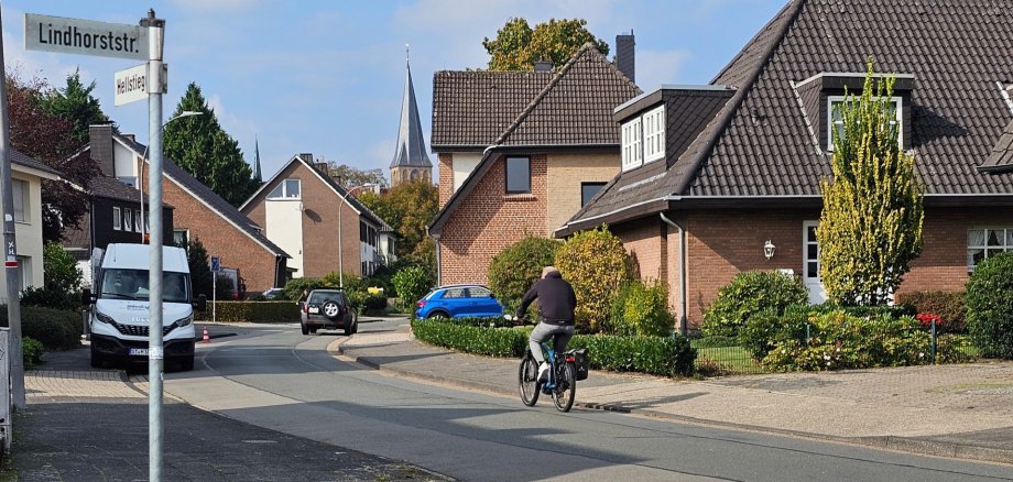 Sie sehen: Kreuzungsbereich von zwei Straßen mit den Straßenschildern, einem Radfahrer und parkenden Autos.