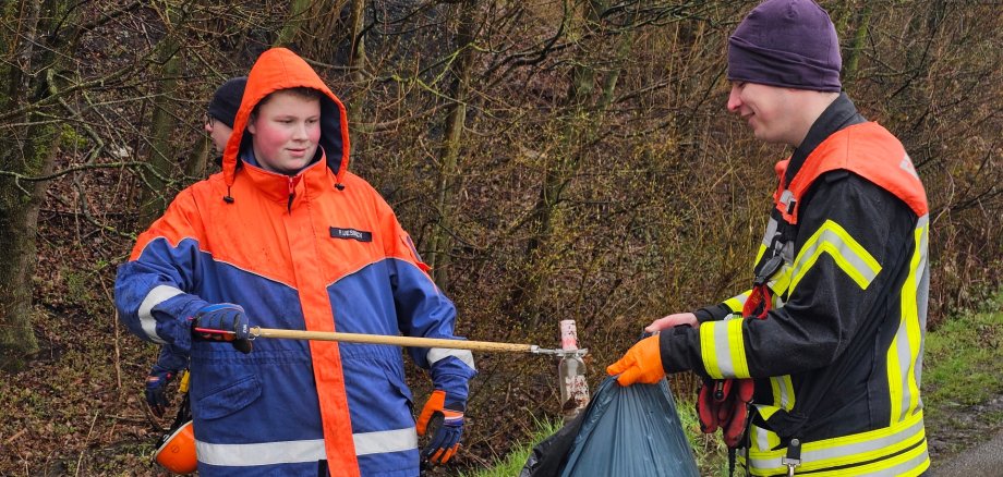 Sie sehen: Zwei Personen, die Müll in einen Sack füllen.