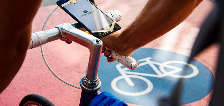 Sie sehen: Einen Fahrradlenker mit Handy in der Halterung auf einem Fahrradweg (Markierung)