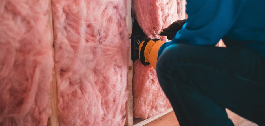Sie sehen: Ein Handwerker setzt Dämm-Material in eine Hauswand ein.