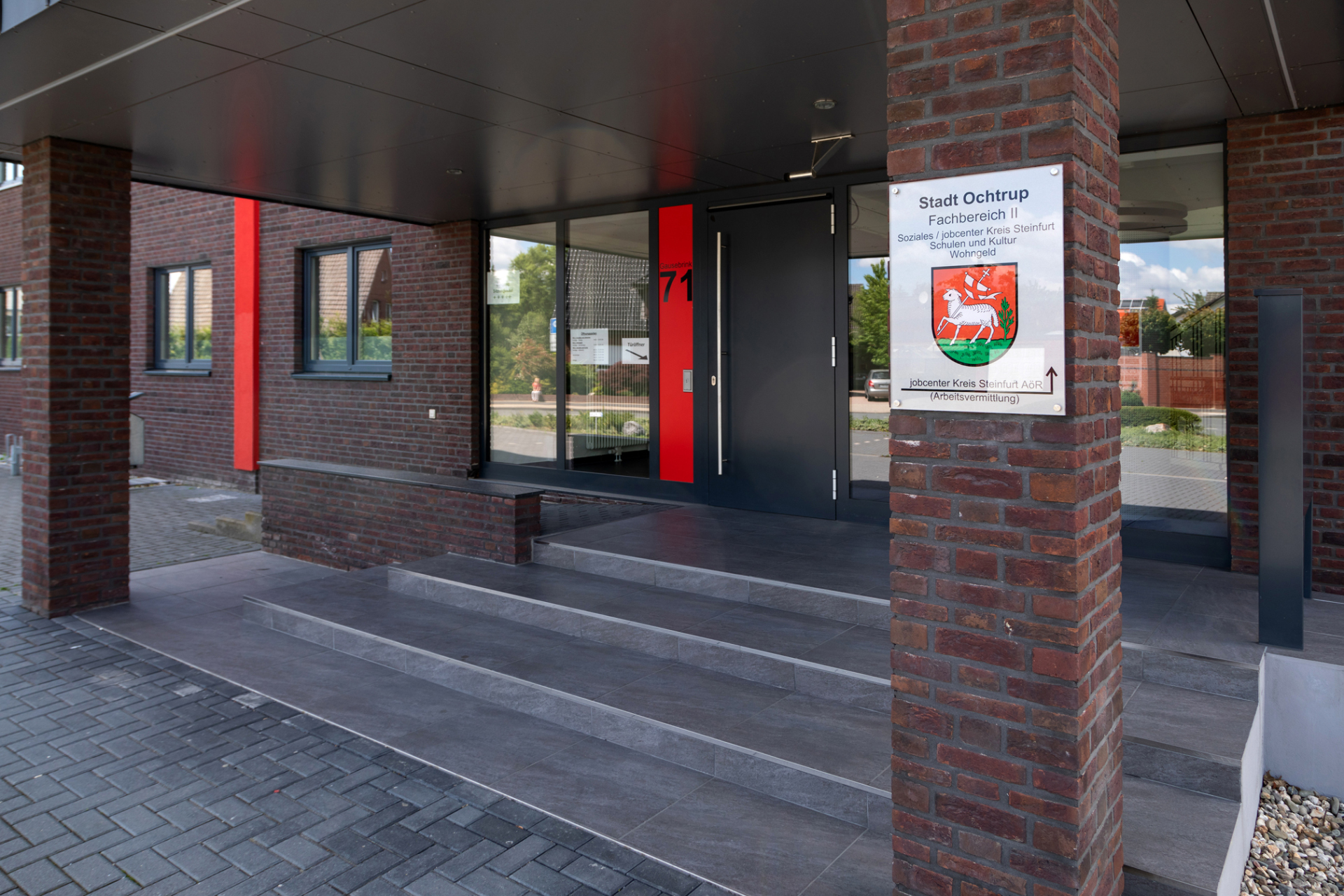 Sie sehen: den Eingangsbereich von Rathaus II mit Treppe, Säulen, Eingangstür und einem Schild