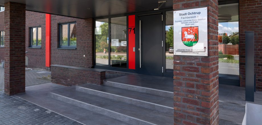 Sie sehen: den Eingangsbereich von Rathaus II mit Treppe, Säulen, Eingangstür und einem Schild