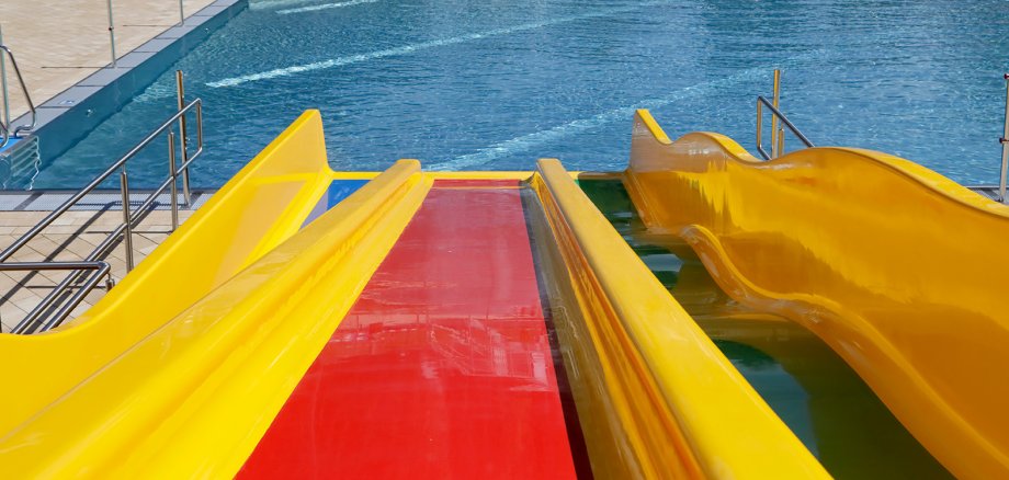 Sie sehen: eine rot-gelbe Wasserrutsche und ein Schwimmbecken von oben