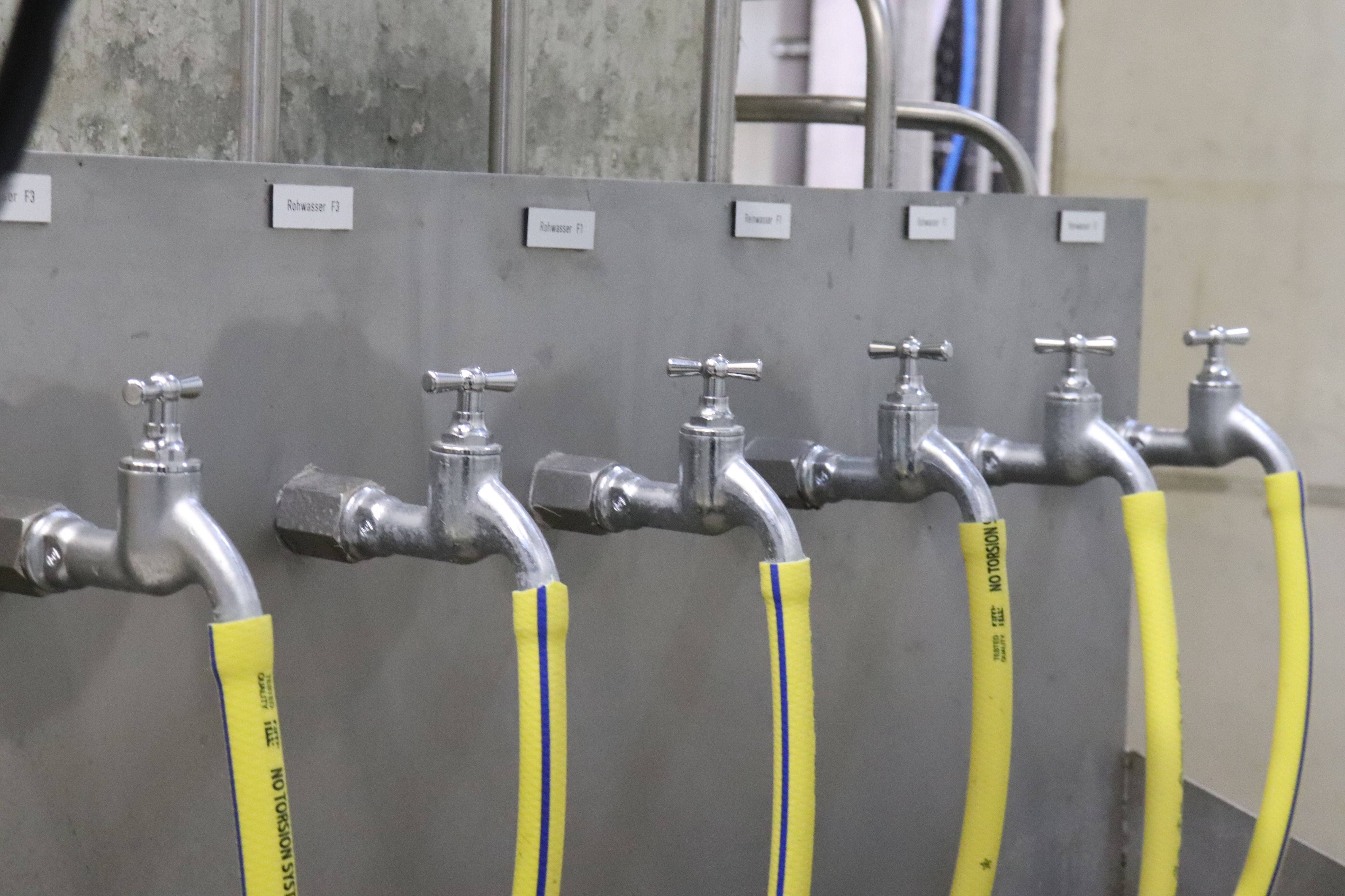 Sie sehen: Sechs Wasserhähne in einer Reihe mit angeschlossenen gelben Schläuchen